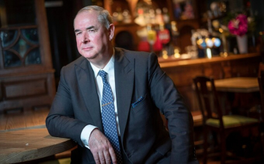 Sir Geoffrey Cox leaning on a bar table, looking pensive.